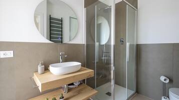 A modern bathroom with a freestanding sink, a glass shower enclosure, and a round mirror on the wall.