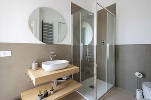 A modern bathroom with a freestanding sink, a glass shower enclosure, and a round mirror on the wall. - CordiAle Suites Pisa (Pisa)