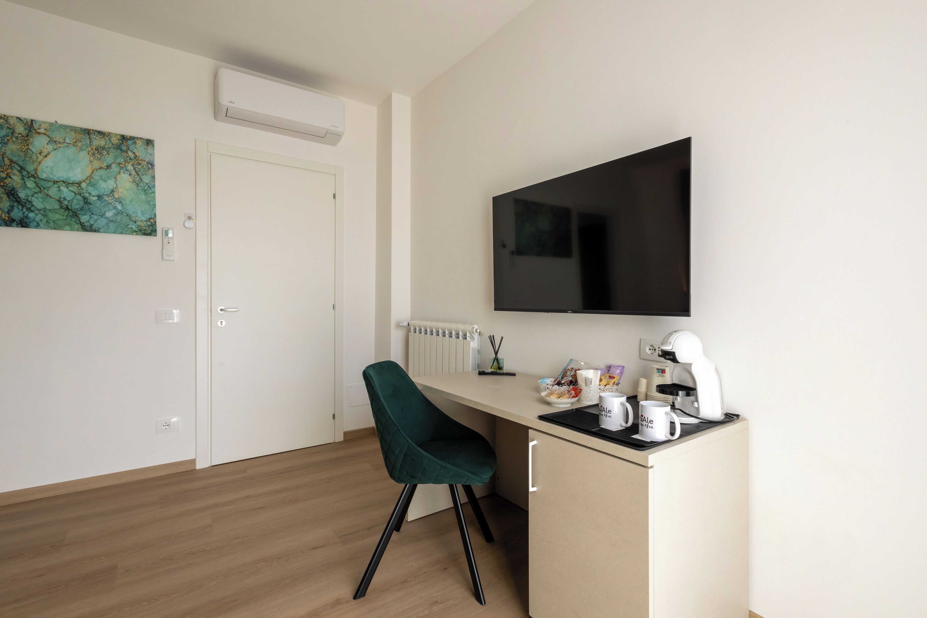 A modern room with a desk, a chair, a mounted TV, a radiator, and a coffee machine.