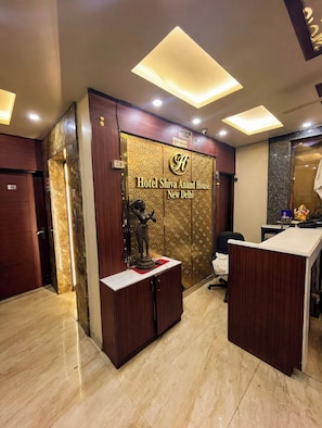 Un espace d’accueil comprenant un comptoir d’enregistrement, un bureau et une enseigne fixée au mur indiquant l’hôtel Shiva Anand House, situé à New Delhi.