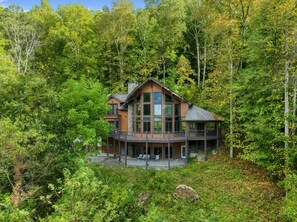 Une cabane à deux étages dotée d’un balcon, entourée d’une forêt dense.