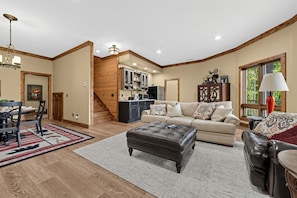 A spacious living room with a leather ottoman, a sofa, and a dining area with a table and chairs. - Mountain-View Home w/ 3 Fireplaces | Sleeps 8 (Maggie Valley)