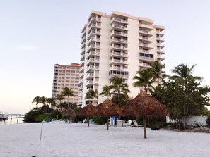 A beachfront hotel with multiple balconies, palm trees, and thatched umbrellas. - One Bedroom Condo with stunning Water Views #1103 (Fort Myers Beach)