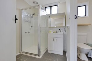Un baño moderno con ducha de vidrio, un lavamanos blanco con artículos de aseo y un inodoro.