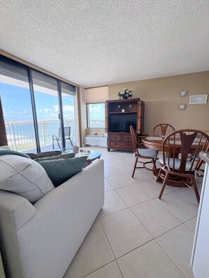 Sala de estar com sofá, mesa de jantar com cadeiras, rack para TV e varanda com vista.