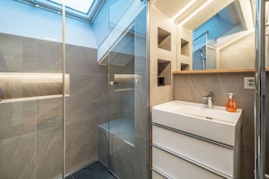 A modern bathroom with a glass shower enclosure, a white sink with a mirror above it, and a skylight above the shower. - Sky Penthouse with matterhorn view (Zermatt)