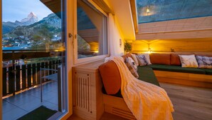 A modern interior with a large window overlooking a mountainous landscape, a wooden floor, and a cozy seating area with cushions. - Sky Penthouse with matterhorn view (Zermatt)
