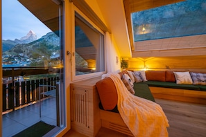 A modern interior with a large window overlooking a mountainous landscape, a wooden floor, and a cozy seating area with cushions. - Sky Penthouse with matterhorn view (Zermatt)