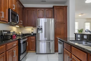 A modern kitchen with wooden cabinets, stainless steel appliances, and a black countertop. - Vista Cay near Epic Apartment remodeled (Orlando)