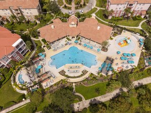 Vista aérea de um hotel com piscina central, várias áreas de descanso e vegetação ao redor.
