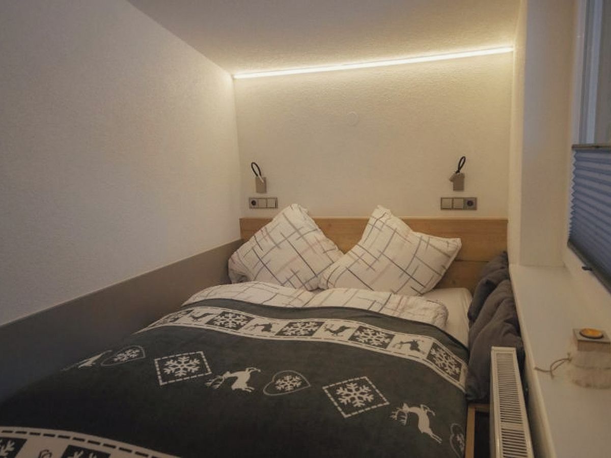 Un dormitorio con cama, dos lámparas de pared, un radiador y una ventana con persianas.