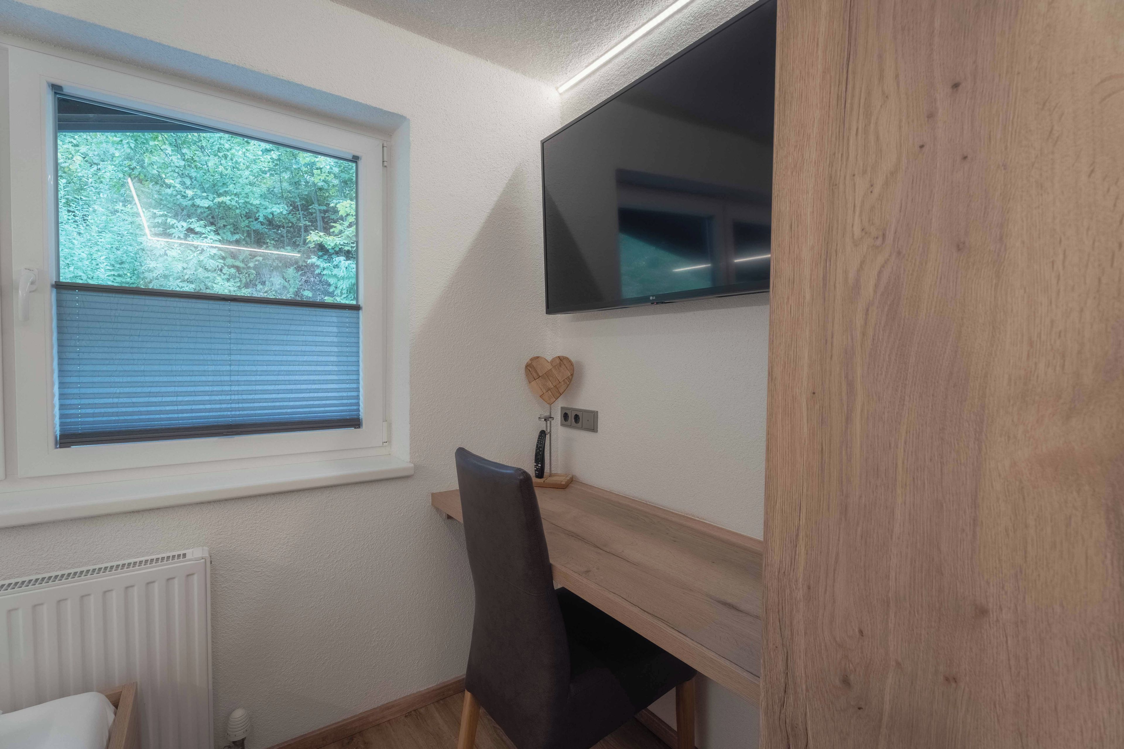 Una habitación con ventana, un escritorio, una silla y un televisor montado en la pared.