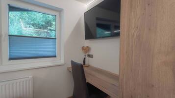 Una habitación con ventana, un escritorio, una silla y un televisor montado en la pared.