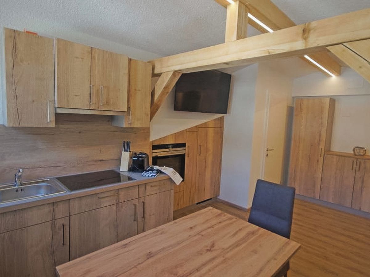 Una cocina con armarios de madera, horno empotrado y una mesa de comedor con sillas.