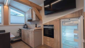 Cocina compacta con gabinetes de madera, horno empotrado, refrigerador y televisor de pantalla plana sobre el horno.