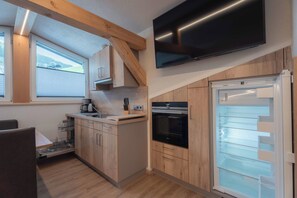 Cocina compacta con gabinetes de madera, horno empotrado, refrigerador y televisor de pantalla plana sobre el horno.