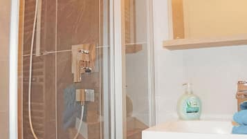 Ein Badezimmer mit einer gläsernen Duschkabine, einem Waschbecken mit Spiegel darüber und einer Seife auf der Ablagefläche.