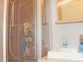 Un baño con ducha envuelta en vidrio, un lavabo con espejo y una botella de jabón en la encimera.