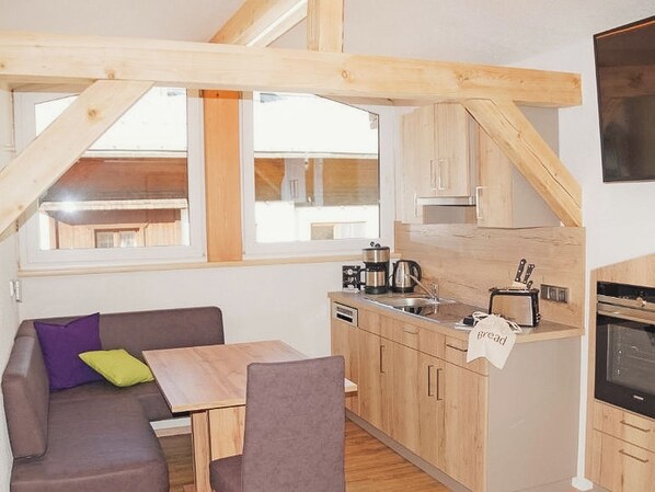 A compact kitchen with wooden cabinets, a dining area with a table and chairs, and a window providing natural light.