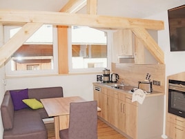 Una cocina compacta con armarios de madera, un área de comedor con mesa y sillas, y un ventanal que proporciona luz natural.