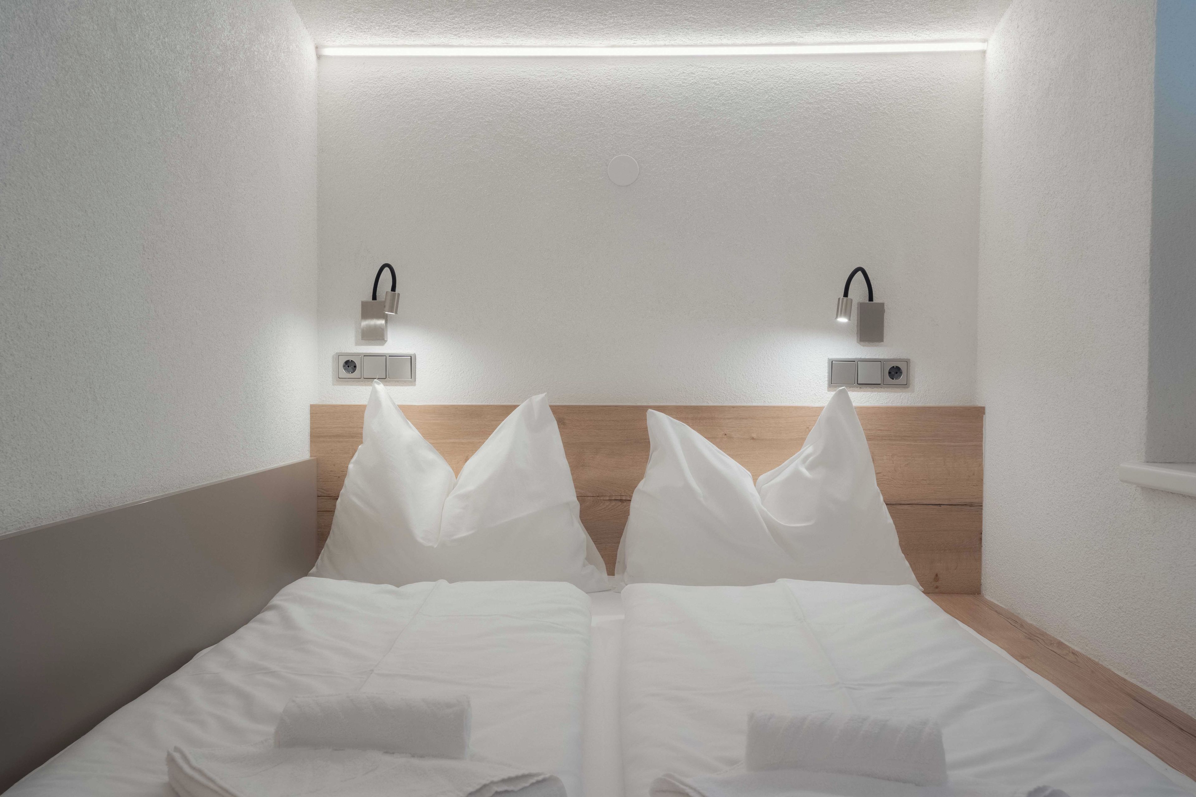 Habitación de hotel con cabecera de madera, dos lámparas de noche y una cama bien hecha con ropa blanca.