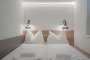 Habitación de hotel con cabecera de madera, dos lámparas de noche y una cama bien hecha con ropa blanca.