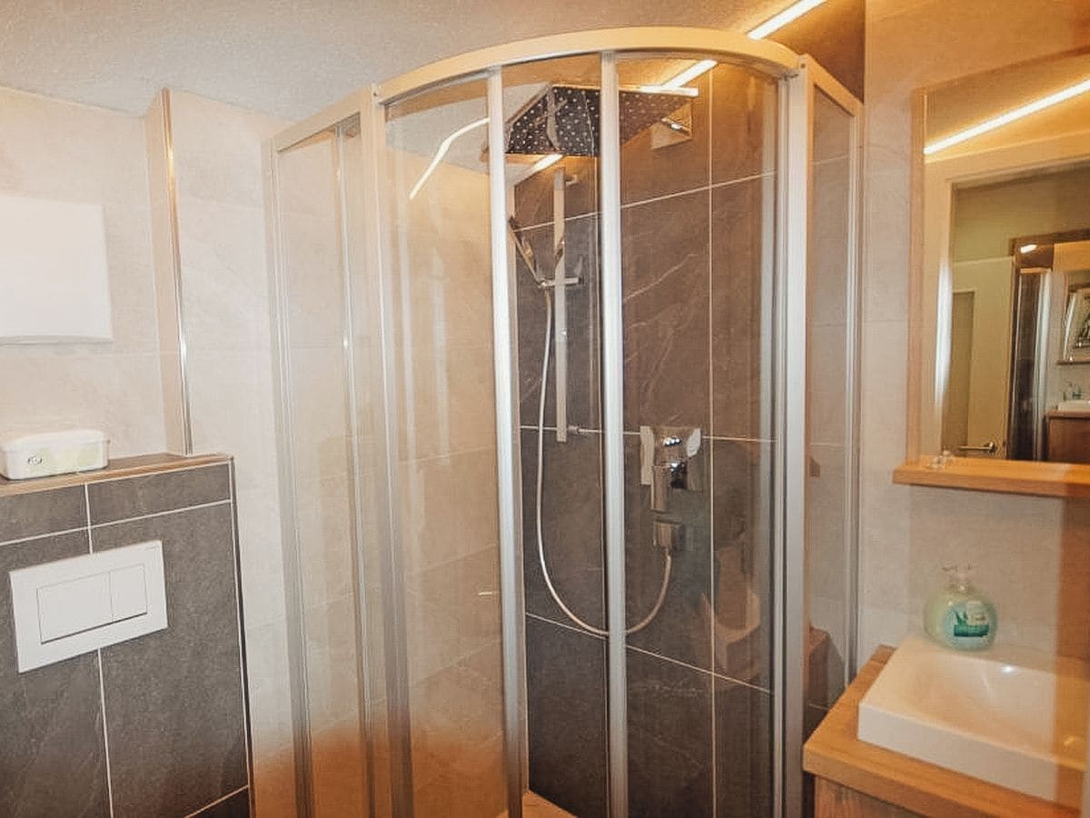 Badekabine med glasdør, et kontrolpanel på væggen og et spejl over vasken.
