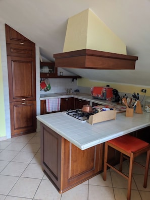 A kitchen with a central island, wooden cabinets, a gas stove, and a red chair. - ELEGANT ACCOMMODATIONS IN AN 18TH-CENTURY PALACE, IDEAL FOR FAMILIES (Alessandria)