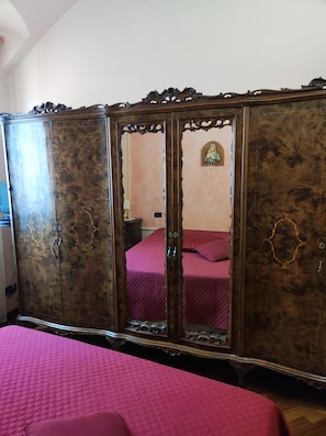 A room with a large wooden wardrobe, a bed with a pink bedspread, and a small bedside table. - ELEGANT ACCOMMODATIONS IN AN 18TH-CENTURY PALACE, IDEAL FOR FAMILIES (Alessandria)