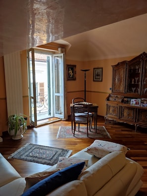 A living room with a sofa, a dining table with chairs, a cabinet with glass doors, and a potted plant. - ELEGANT ACCOMMODATIONS IN AN 18TH-CENTURY PALACE, IDEAL FOR FAMILIES (Alessandria)