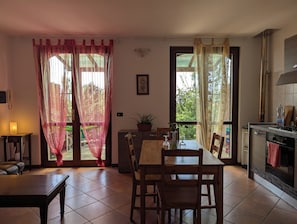 Un comedor con mesa y sillas, una planta en maceta y vistas al exterior con vegetación.