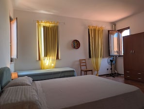 Un dormitorio con cama, una silla, un radiador, un ventilador y un armario.