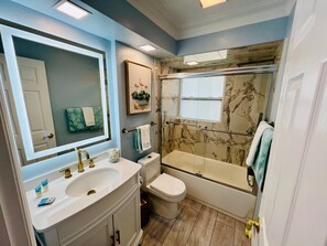 Een badkamer met een grote spiegel, een witte wastafel, een toilet en een bad met glazen douchewand.