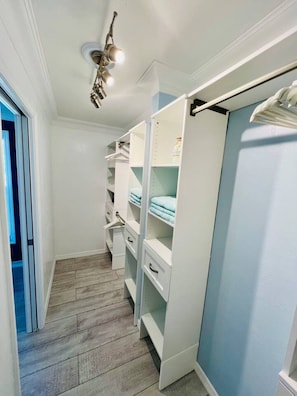 A narrow hallway with a closet containing open shelves and drawers, a ceiling light fixture, and a wooden floor. - Your Private Florida Escape - Stunning Pool Home (Fort Myers Beach)