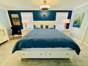 Een slaapkamer met een bed, twee nachtkastjes, een stoel en een schilderij aan de muur.