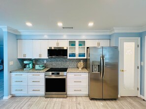 A modern kitchen with white cabinets, a stainless steel refrigerator, and a granite countertop. - Your Private Florida Escape - Stunning Pool Home (Fort Myers Beach)