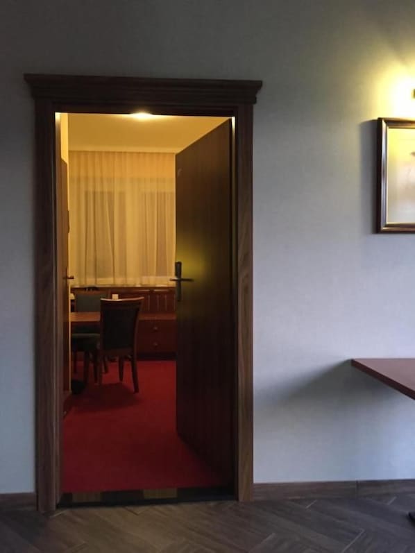 A doorway leading to a room with a dining table and chairs, a red carpet, and a framed picture on the wall.