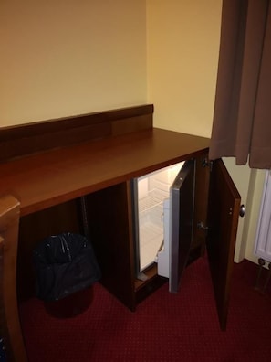 A room with a wooden desk, a trash bin, and a door leading to a white room.