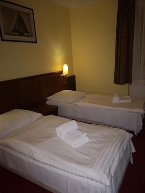 A hotel room with two beds, a nightstand, a lamp, and a painting on the wall.