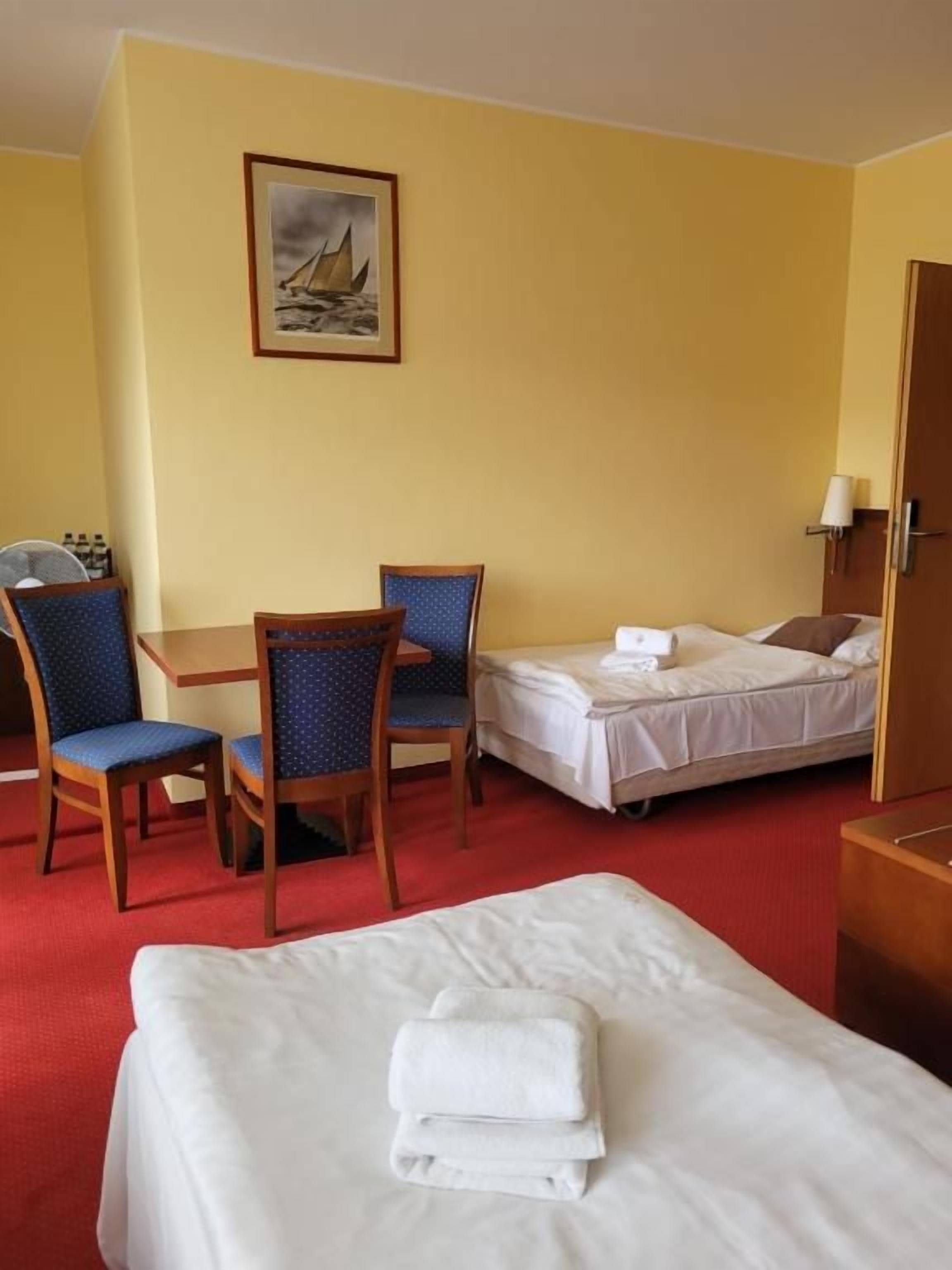 A hotel room with a bed, a desk with two chairs, a bedside table, and a wall-mounted lamp.