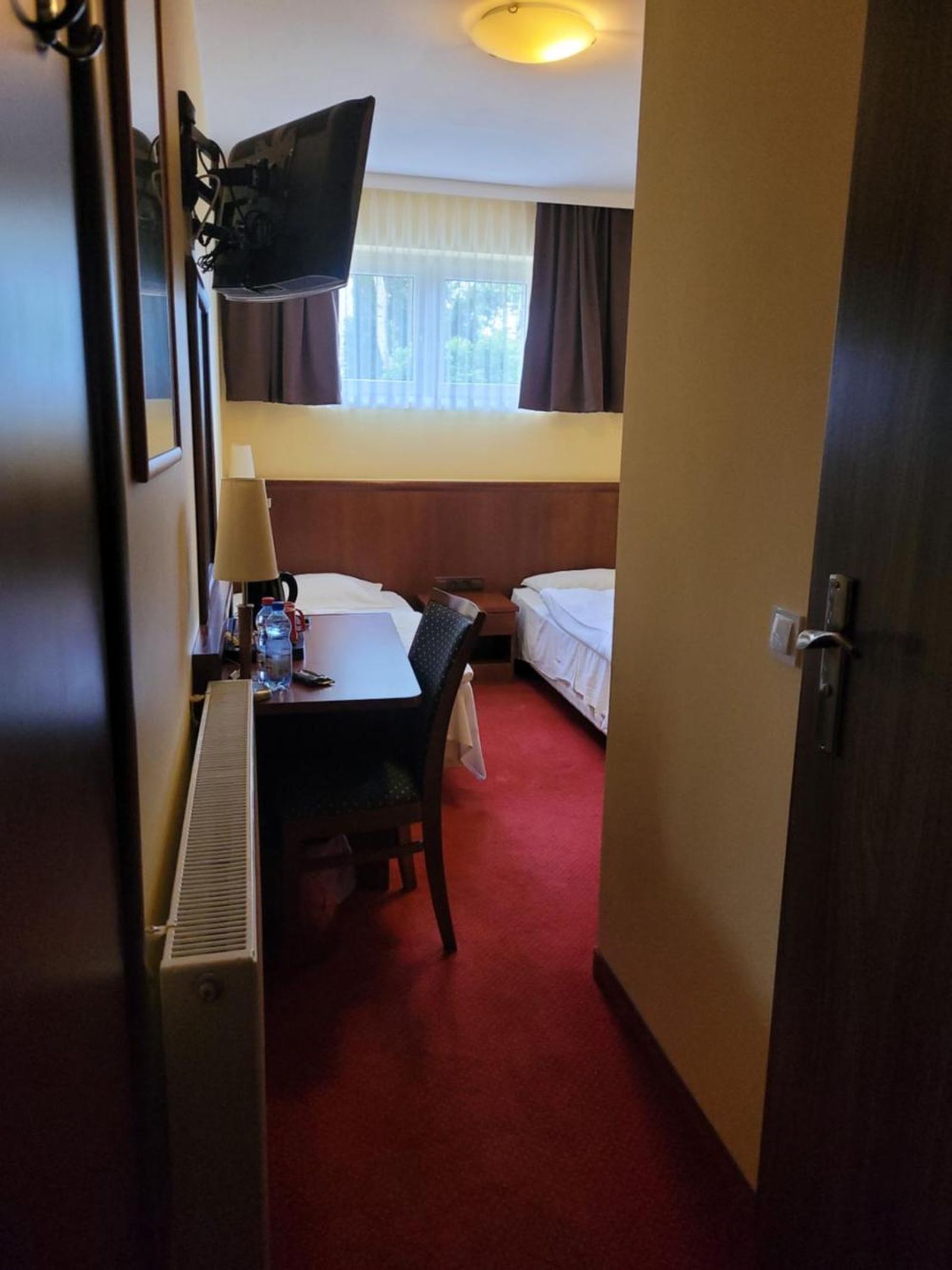 A hotel room with a desk, chair, two beds, a TV, and a window with curtains.