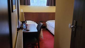 A hotel room with a desk, chair, two beds, a TV, and a window with curtains.