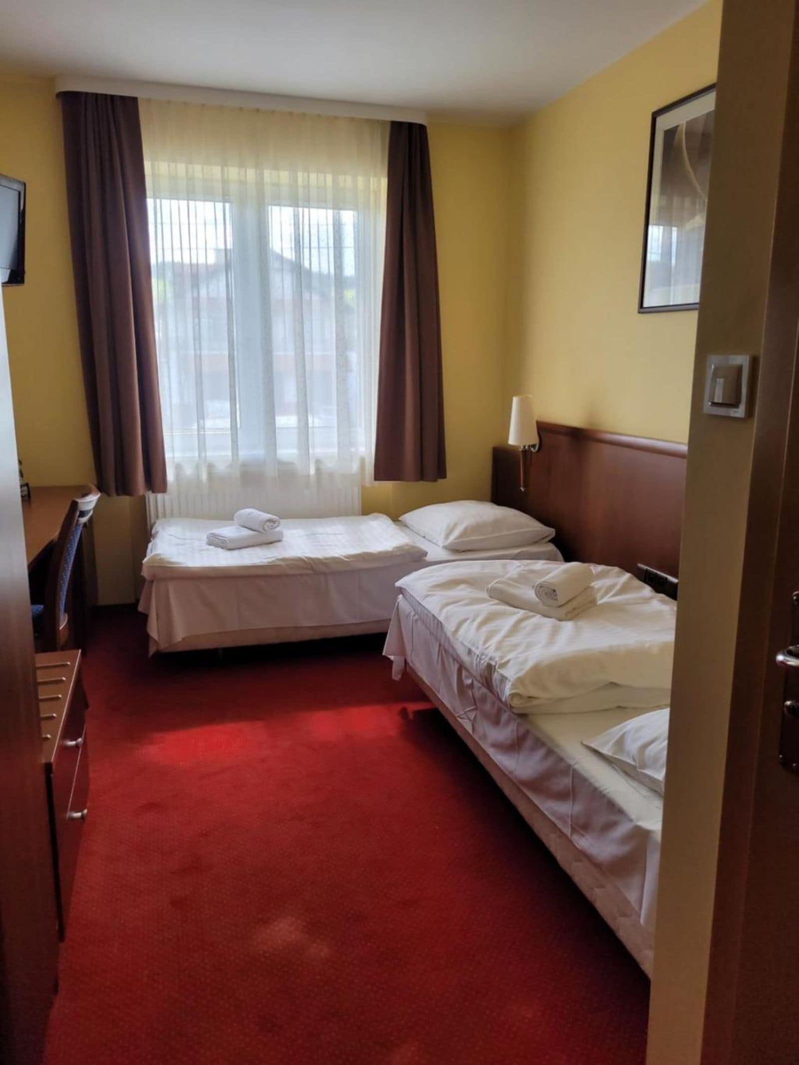 A hotel room with two beds, a desk, and a window with curtains.