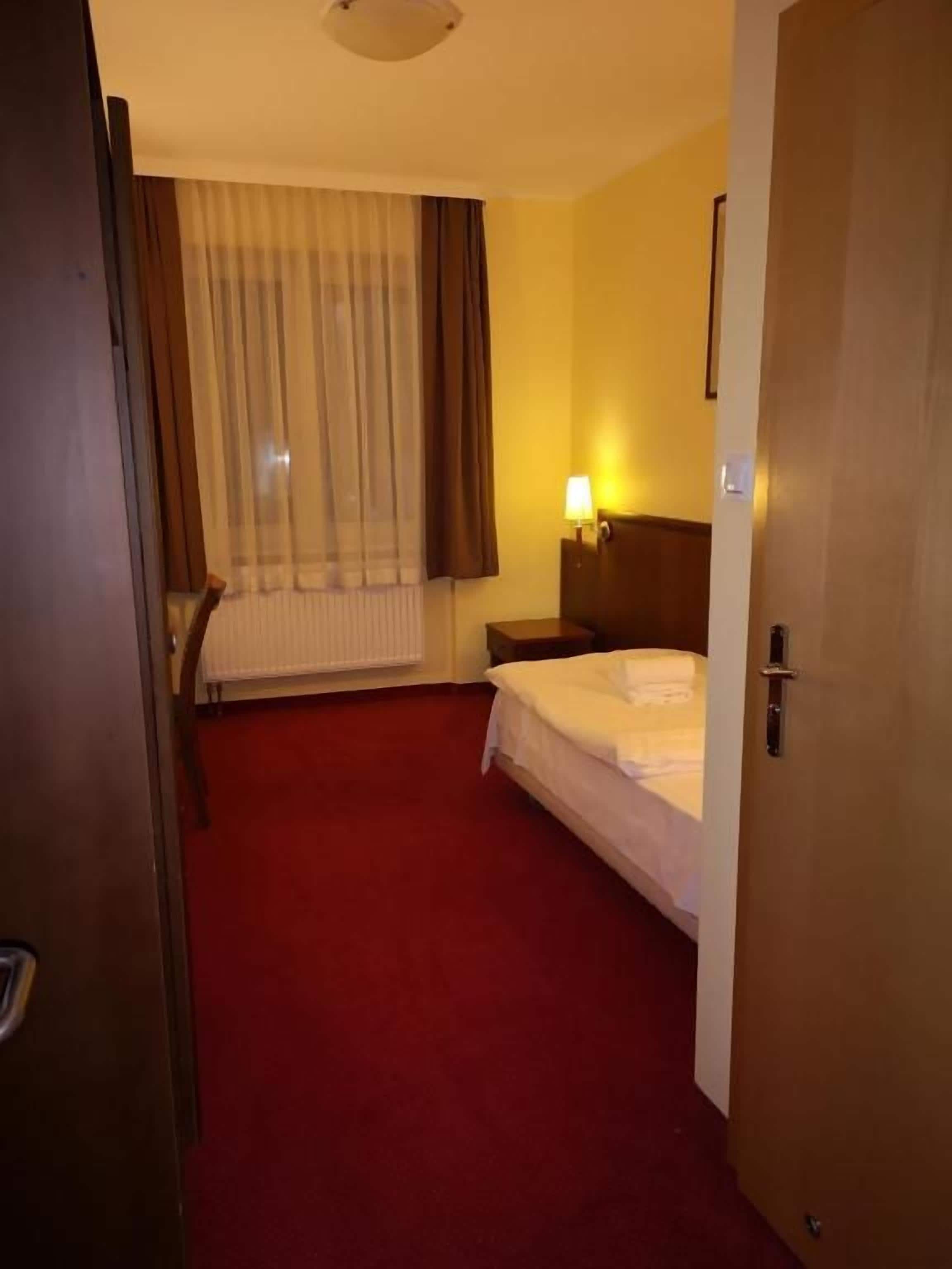 Una habitación de hotel con una cama, una mesita de noche, una lámpara, una ventana con cortinas y una puerta.