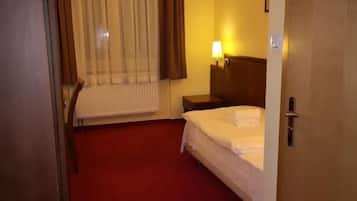 Una habitación de hotel con una cama, una mesita de noche, una lámpara, una ventana con cortinas y una puerta.