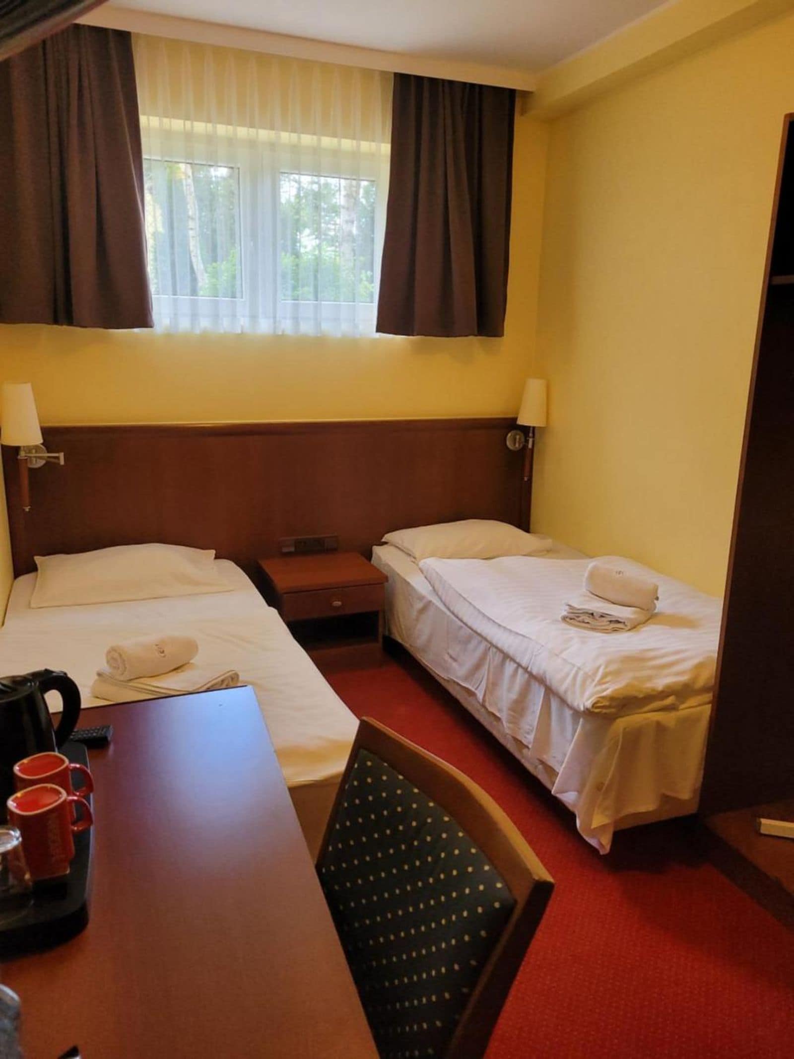 Ein Hotelzimmer mit zwei Betten, einem Schreibtisch mit Wasserkocher und einem Stuhl.