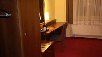 Ett hotellrum med en garderob i trä, ett skrivbord med en lampa, en tv på väggen och en röd matta.