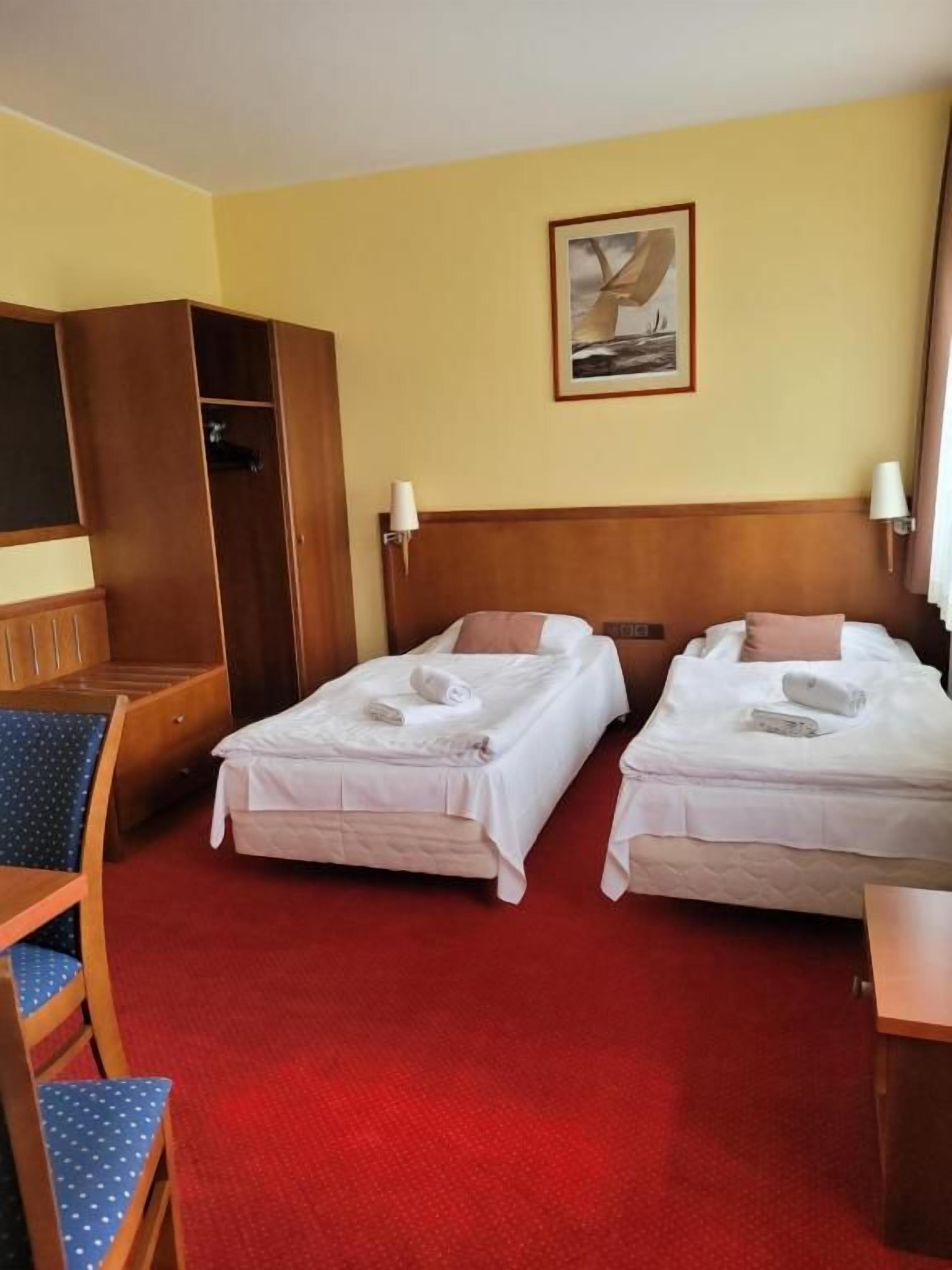 A hotel room with two beds, a wooden wardrobe, a desk, and a chair.