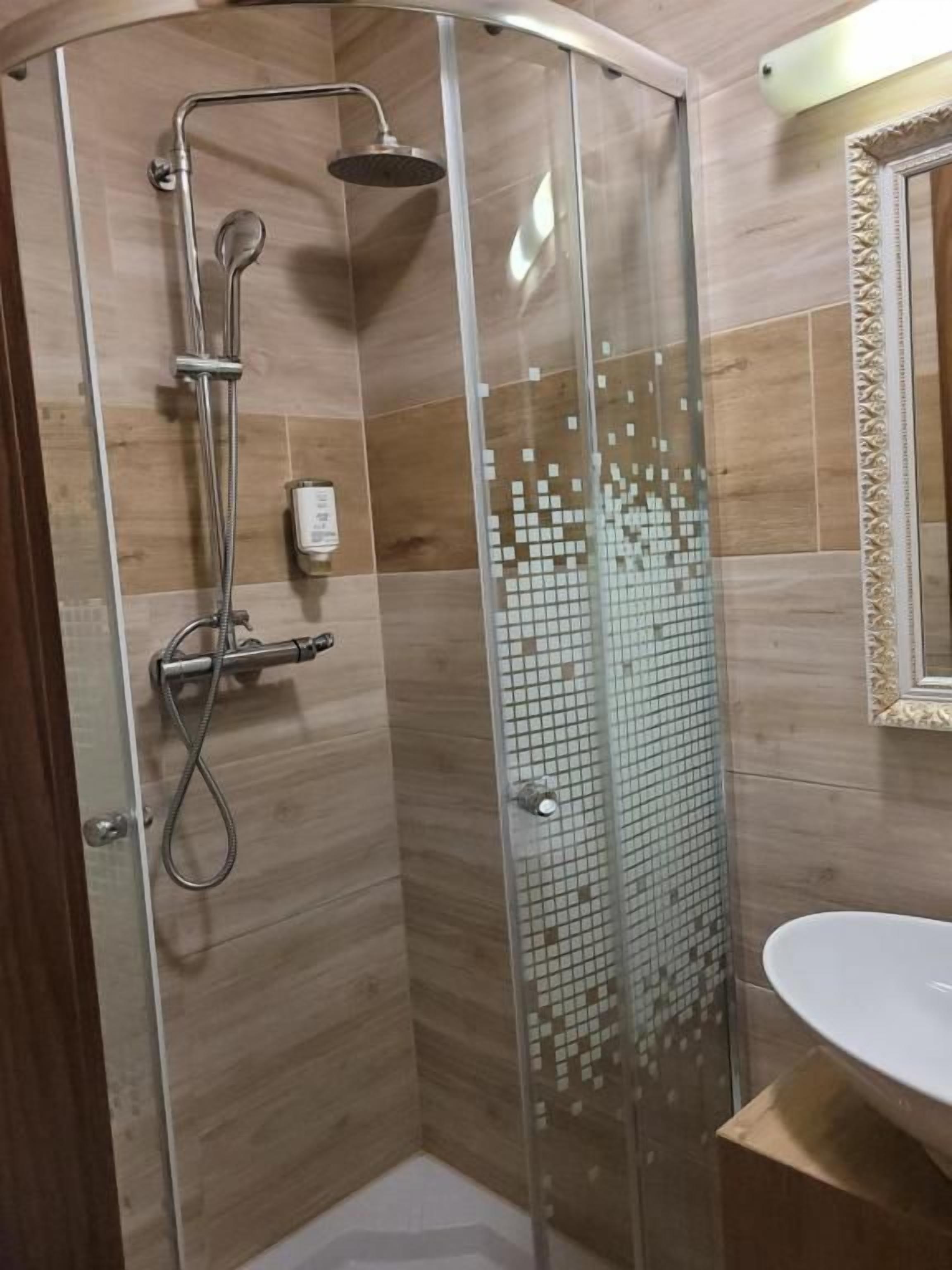 Una ducha con puerta de vidrio, cabezal de ducha de mano y panel de control en la pared.