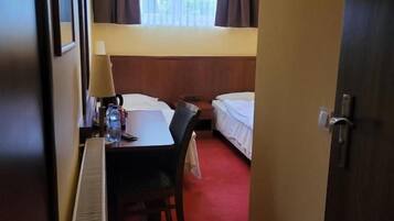 Una habitación de hotel con cama, escritorio con silla, televisor montado en la pared y ventana con cortinas.